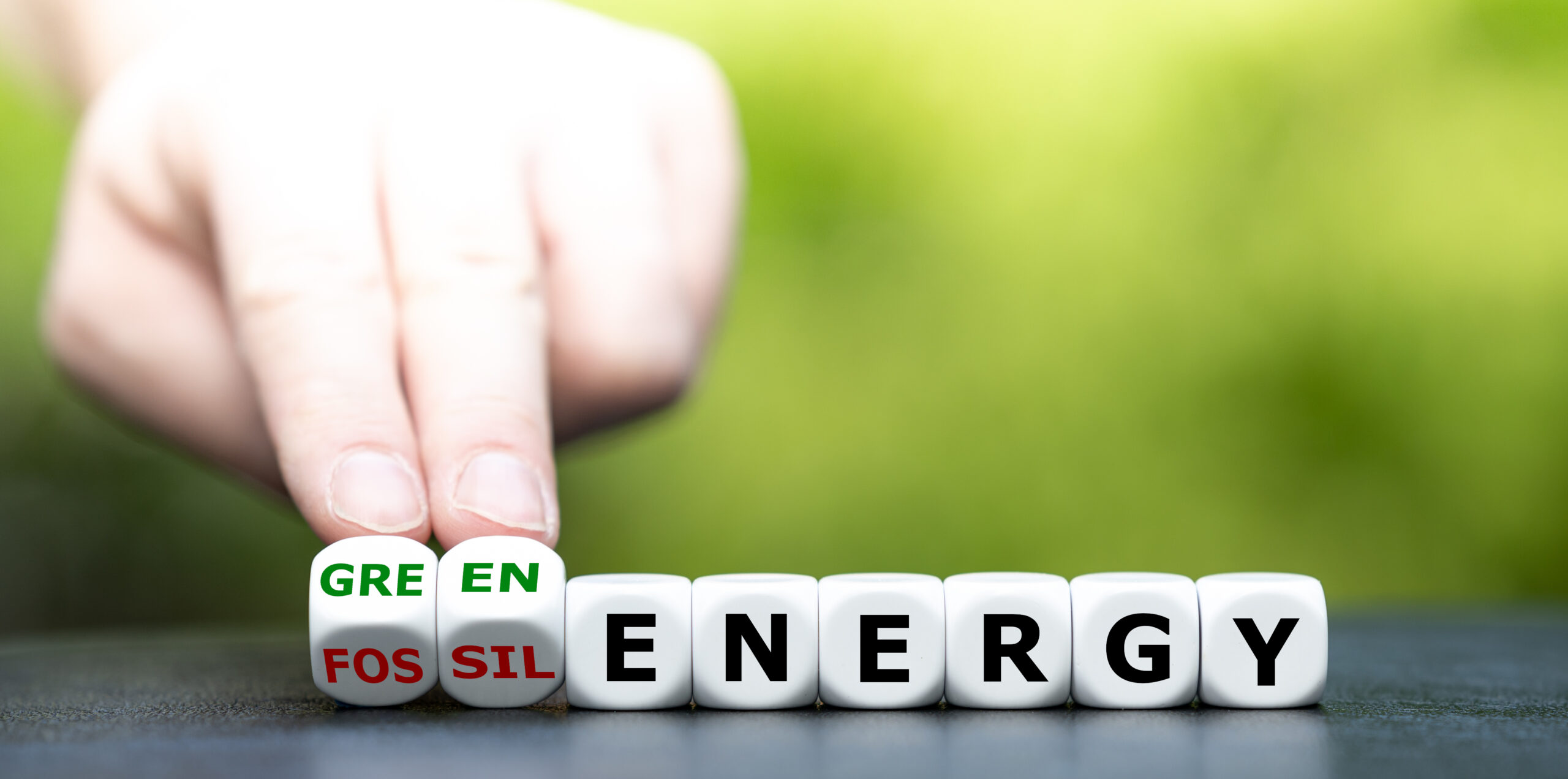 image symbolisant la transition énergétique. Sur des dés est écrit : Energy. Sur deux autres dés le mot "fossil" laisse place au mot "green".